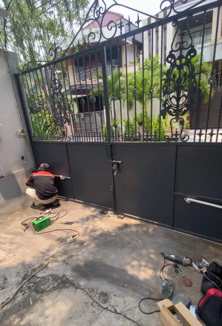 Teknisi mengerjakan instalasi sistem penggerak gerbang swing otomatis dua daun