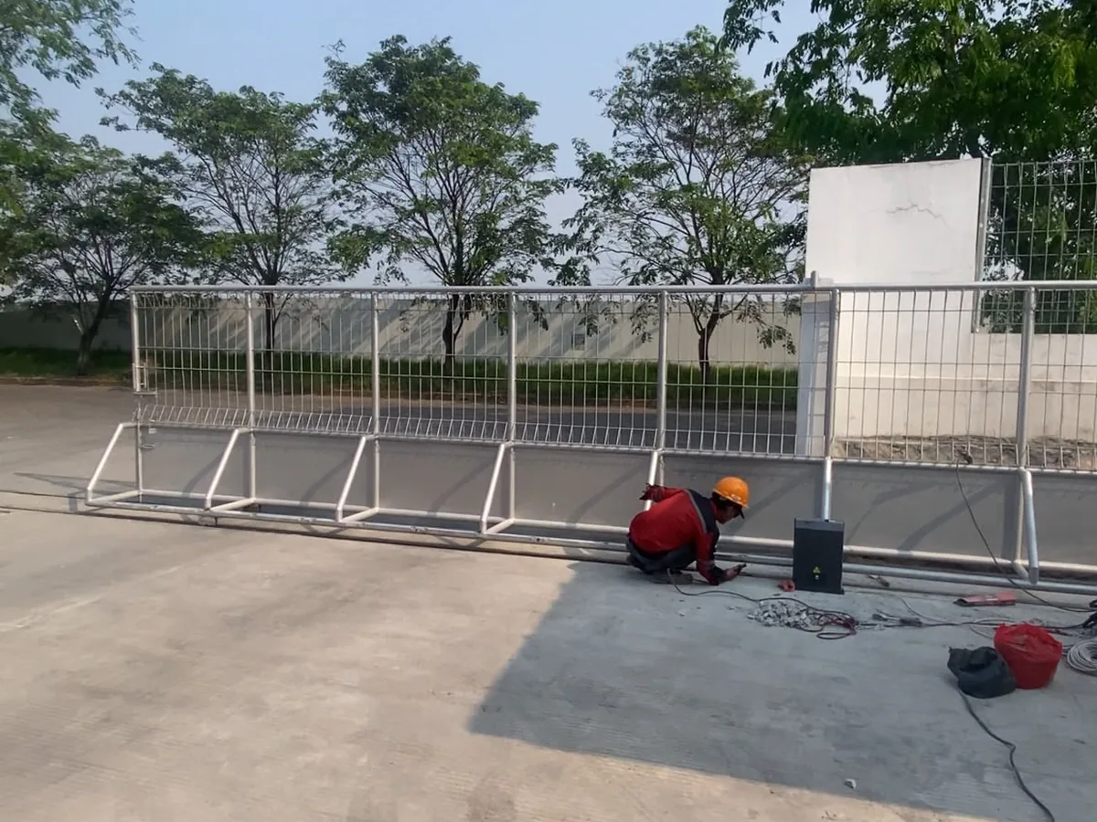 Teknisi melakukan instalasi motor pagar sliding otomatis pada gerbang besi berukuran besar